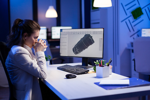 A woman seated at a desk, focused on her computer screen, with a notepad and pen beside her.3d Modelling Service